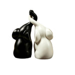 Matte black and white couple elephant figurines with raised trunks forming a heart on white