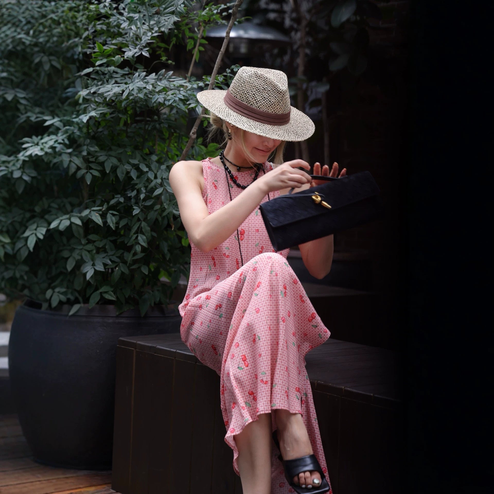 Woman seated in pink cherry gingham silk dress holding a black clutch