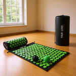 Black spiked mat with green spikes on a wooden floor beside a spiked pillow, a black bag and two spiked balls