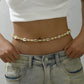 Cowrie shell and bone tone disc waist chain on a cord, worn low over light washed jeans