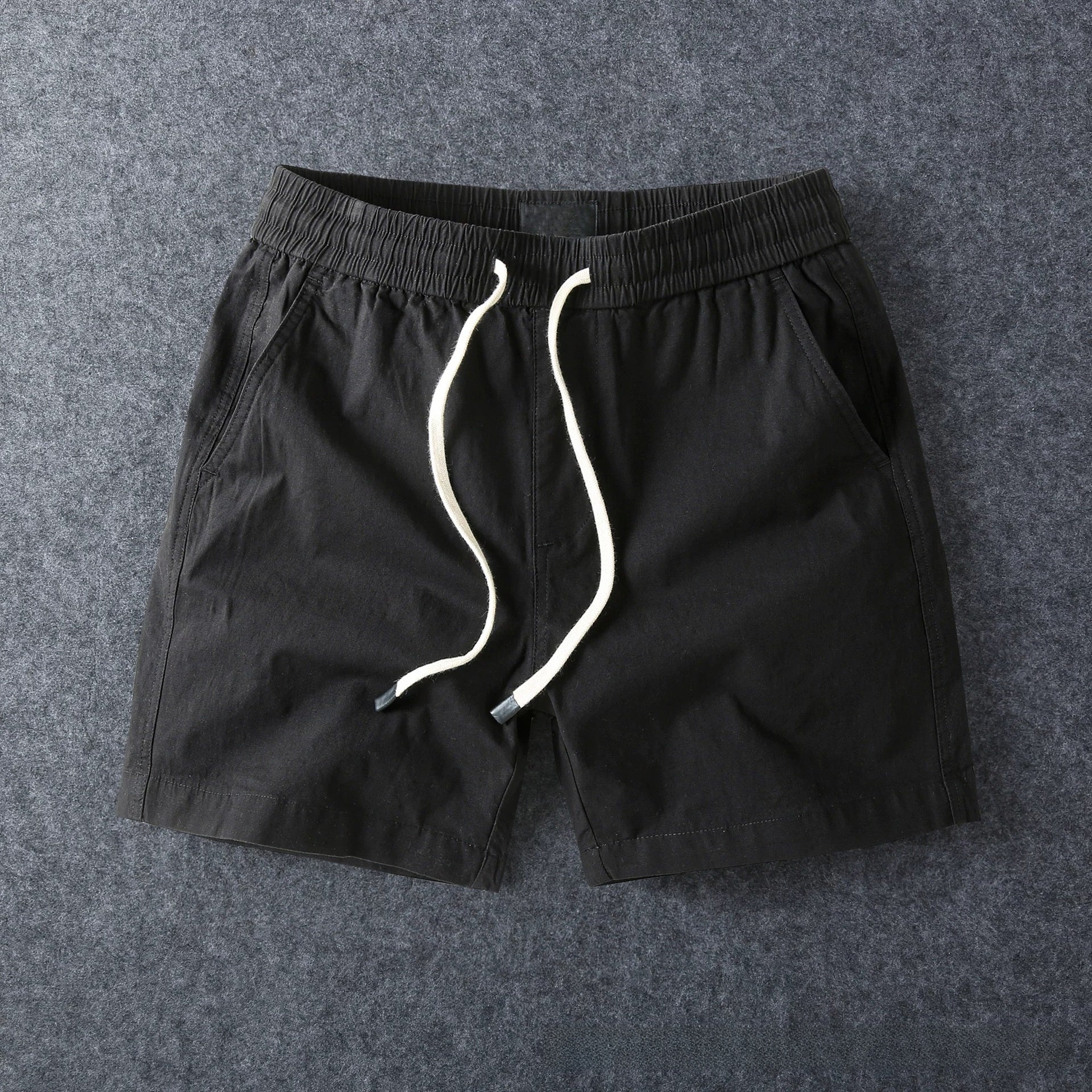 Black men's cotton drawstring shorts laid flat with the drawstring untied