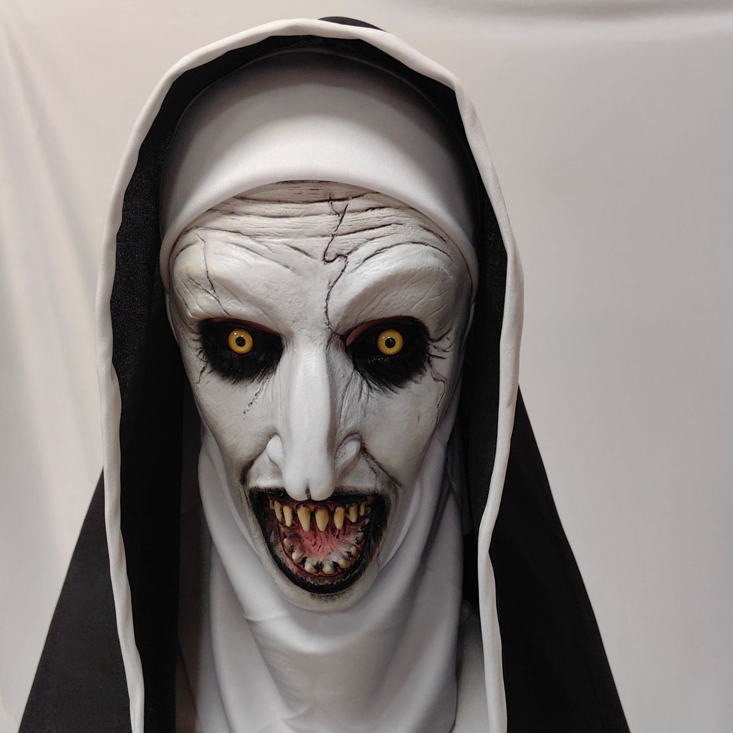 Pale horror nun costume mask with yellow eyes framed by a nun style veil