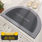 Gray semi-circular diatomite bath mat with a dark center and SHOWER ROOM text on a tiled floor beside two slippers
