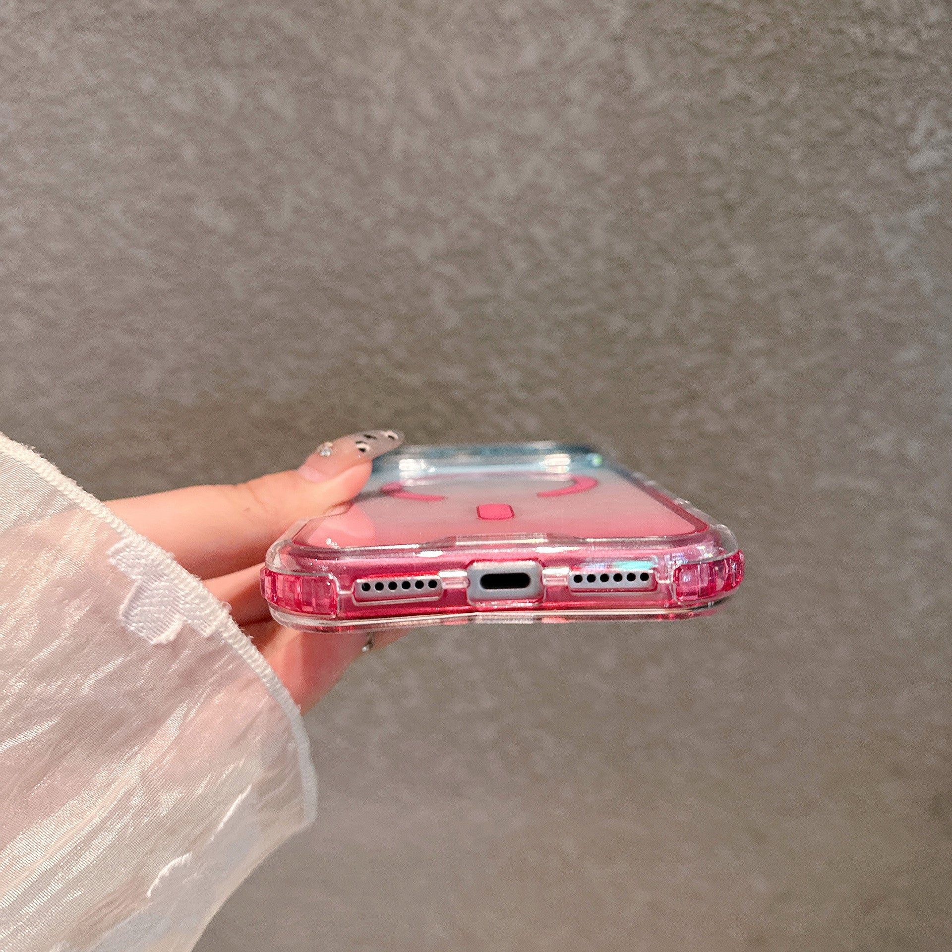 Bottom edge of a pink gradient clear case, speaker cutouts and charging port opening in view