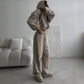 Woman in a taupe khaki hoodie set with the hood up and wide leg trousers, standing beside a sofa