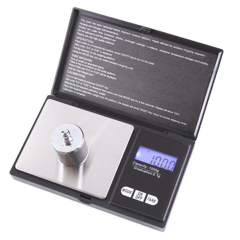 Open pocket scale with a round calibration weight on the platform, display labeled 1000 g capacity and 0.1 g