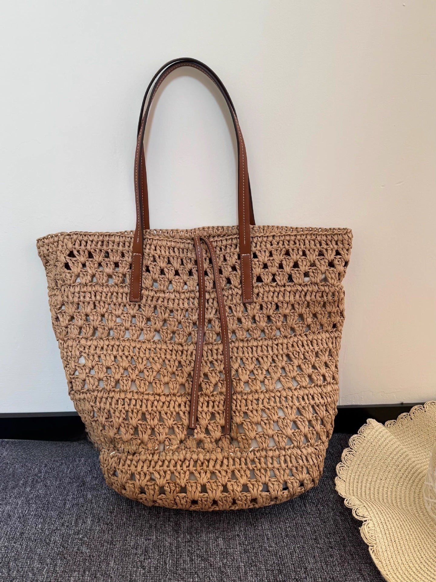 Natural straw tote bag photographed in soft studio light against a plain backdrop
