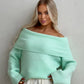 Mint green off-shoulder fold-over knit sweater with wide cuffs worn with white trousers