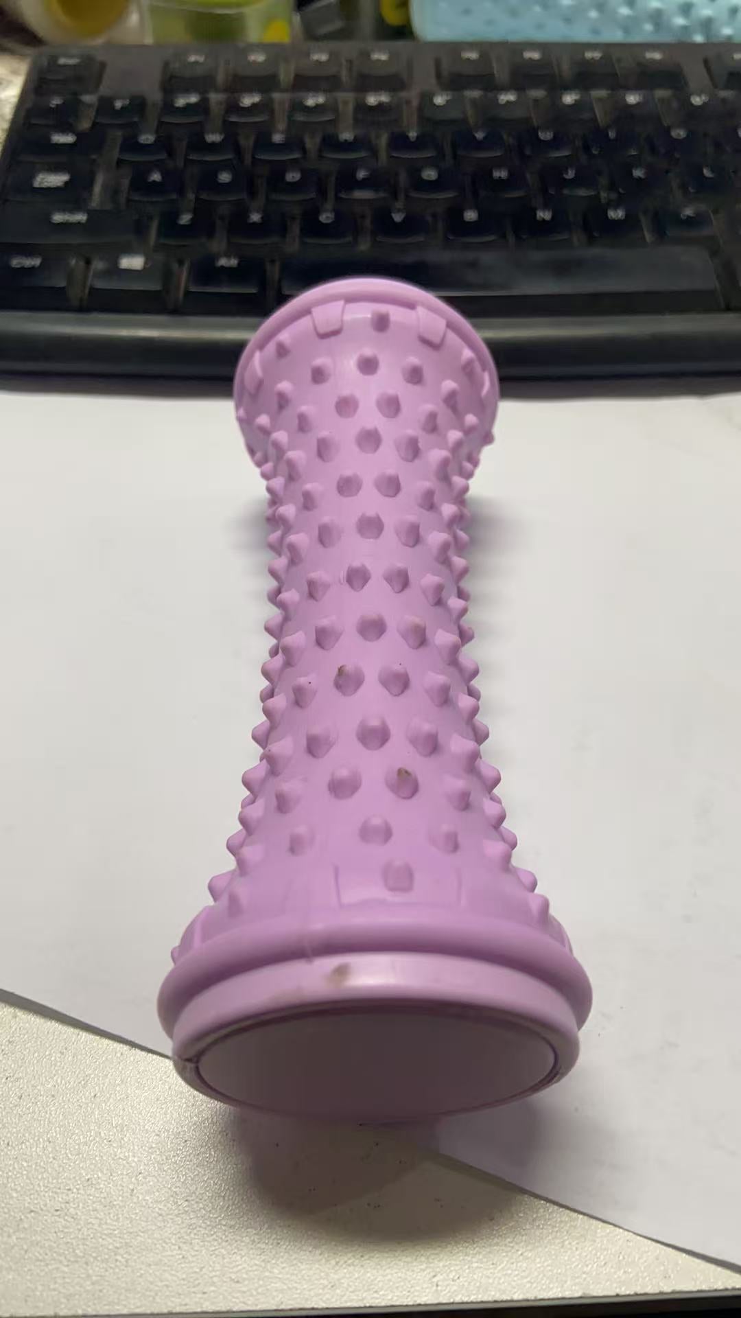 Purple nubbed foot roller standing upright on a desk beside a keyboard