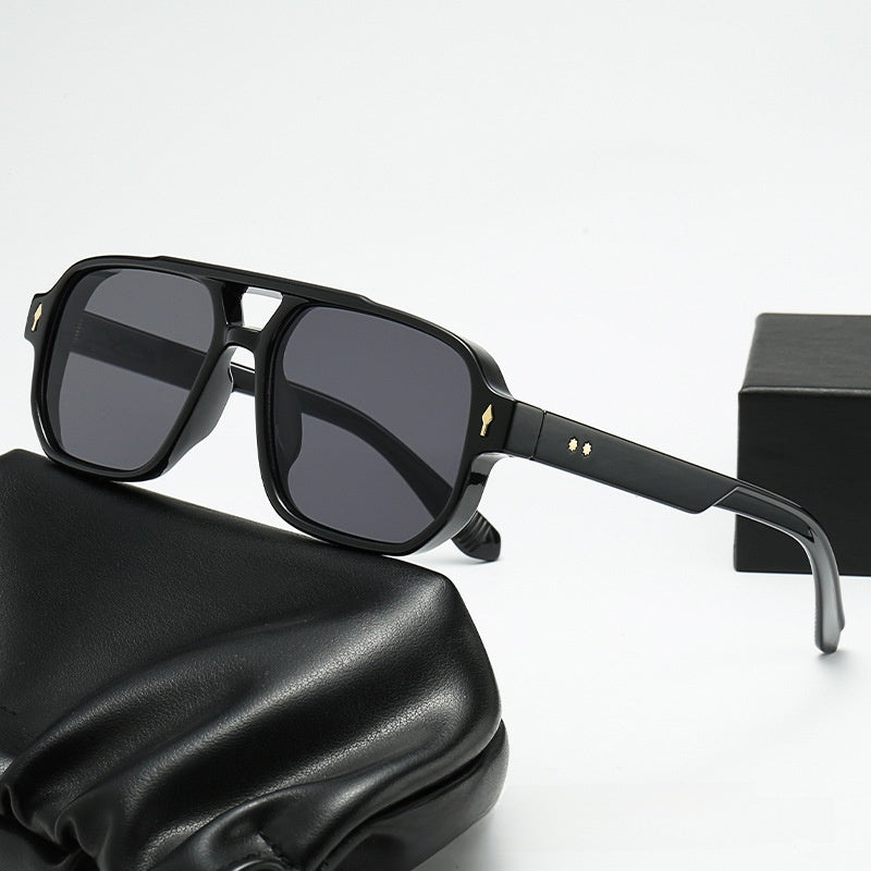 Square double bridge sunglasses with a black frame and gray lenses on a black case