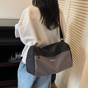 Woman wearing a black duffel bag with a gray grid panel across the body on a long strap, seen from behind