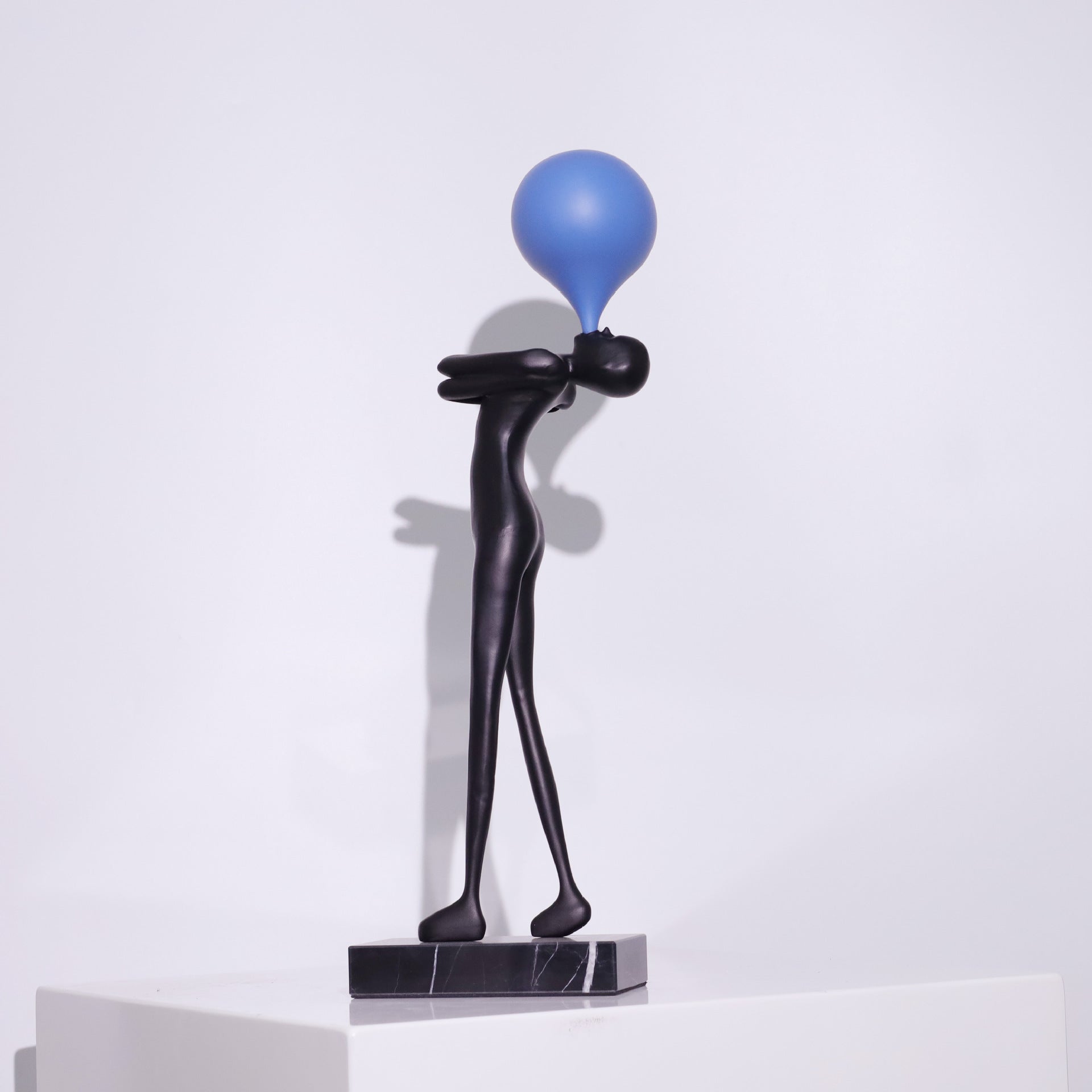 Modern balloon figure statue shown at an angle, long black body with a colored balloon and marble foot