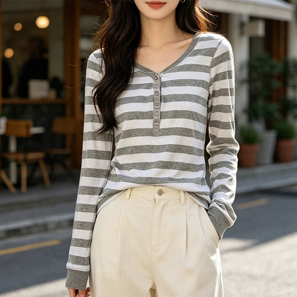 Woman in a gray and white striped henley top with cream trousers outside a cafe, three quarter front view