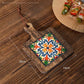 Wood trivet with an orange and blue rosette tile on planks, marked 20 cm by 14 cm