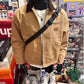 Khaki zip-up jacket with brown collar worn with a black crossbody bag, front view with chest pocket