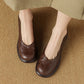Pair of brown embossed leather round toe slip-on shoes seen from above, one worn on a foot