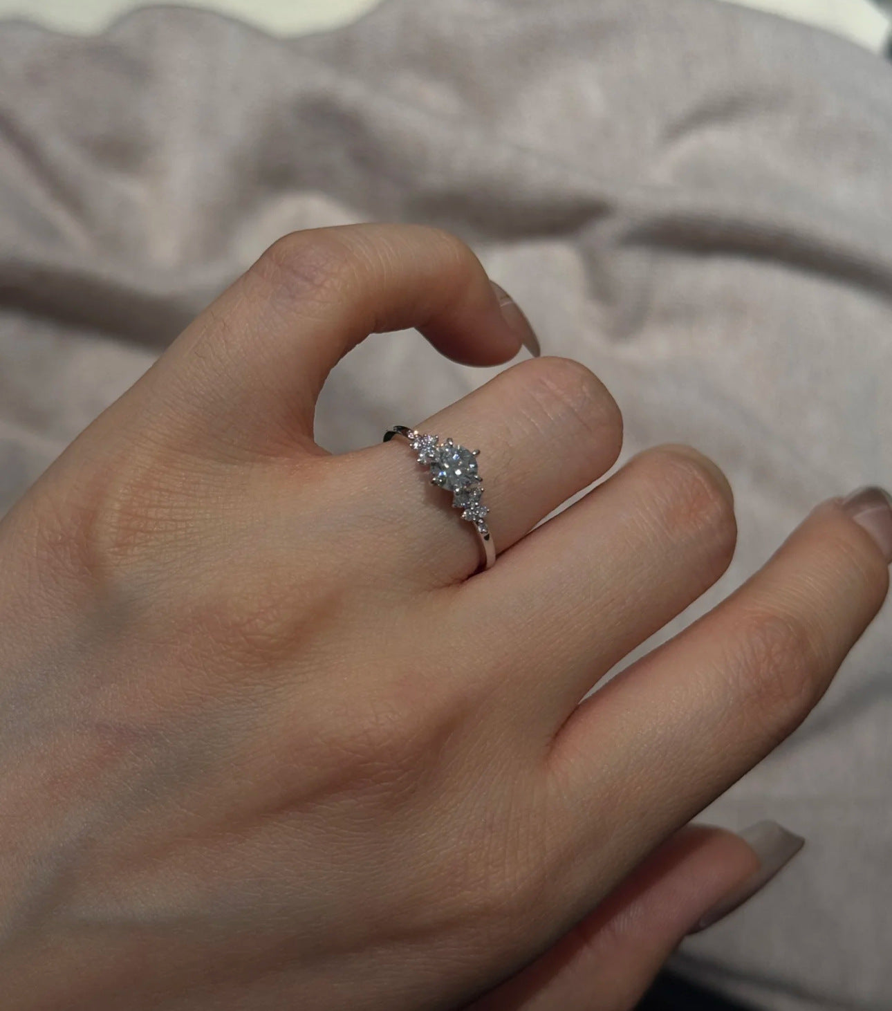 Silver cubic zirconia cluster ring worn on the hand, slim band with a bright round center stone and side accents