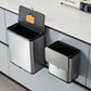 Open stainless steel trash can with an orange insert box in the lid beside a closed one on a cabinet door
