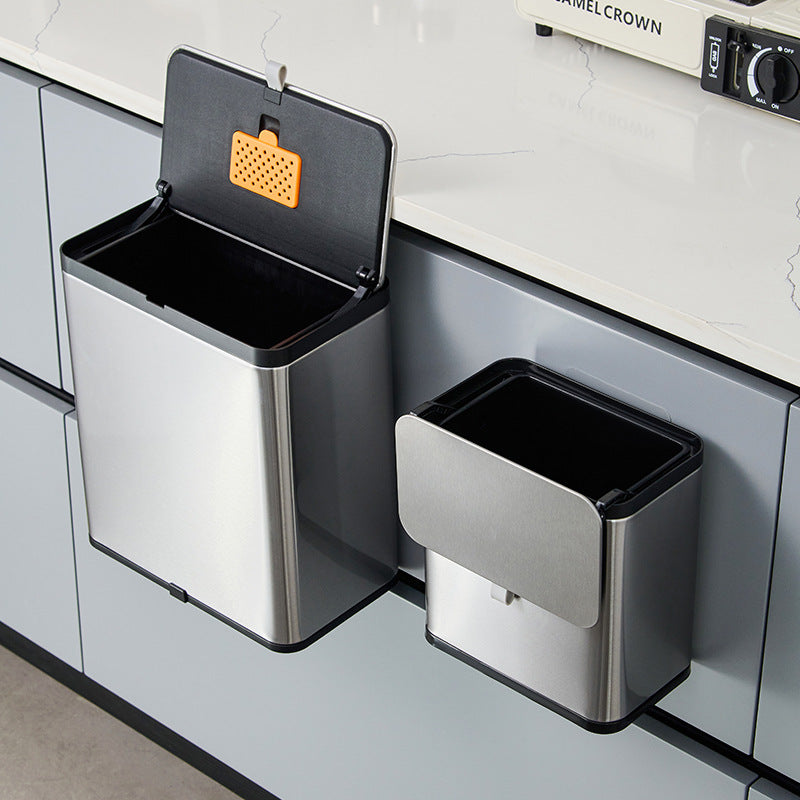 Open stainless steel trash can with an orange insert box in the lid beside a closed one on a cabinet door