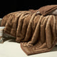 Camel option: camel brown vegan fur blanket with a brown border, draped over a bed on a dark background