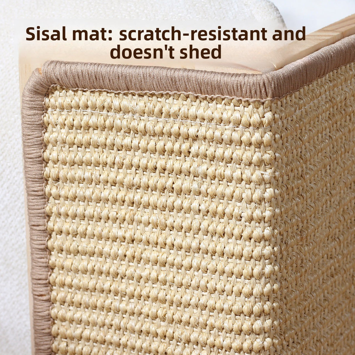 Close view of woven sisal scratching surface with taupe edge binding and a solid wood frame beside a cream sofa