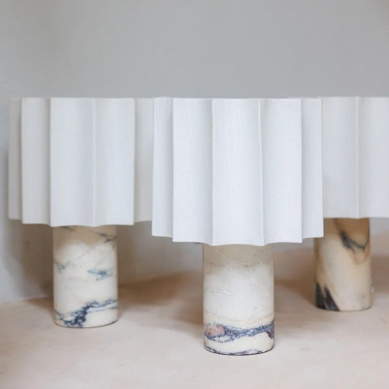 Warm lit marble table lamp with a fluted linen shade in a styled room