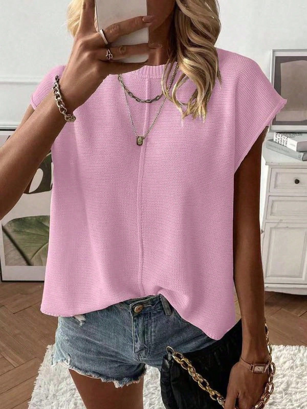 Woman wearing a solid color round neck cap sleeve knit top with a relaxed drape over denim shorts
