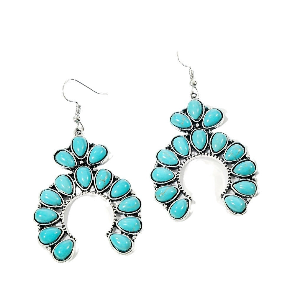 Pair of silver tone crescent drop earrings with turquoise colored teardrop stones on a white background