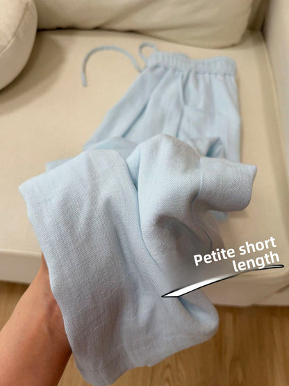 Light blue cotton linen straight-leg pants folded on a beige sofa, petite short length