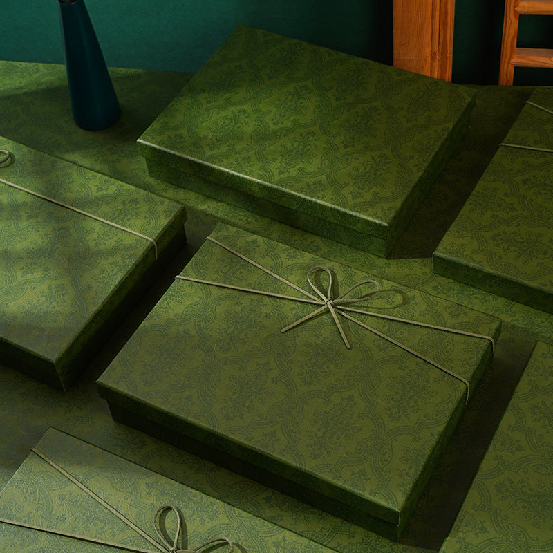 Olive green damask gift boxes with cord bows on a green table in front of a green wall