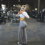 Grey high-waist wide-leg flared yoga pants worn with a white crop top, gym mirror selfie side view