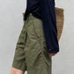 Walking side view of knee-length olive green Bermuda shorts with deep cuffed hem