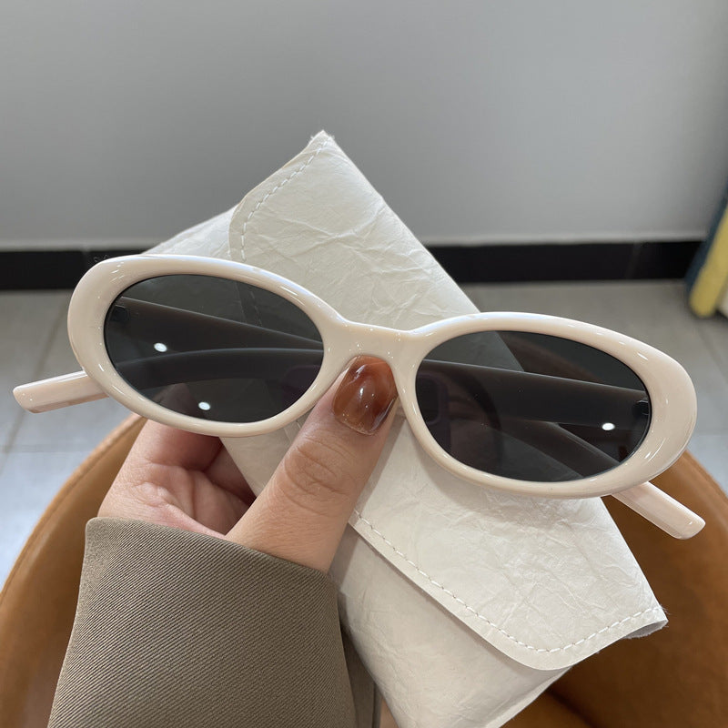 Off-white oval frame sunglasses with gray lenses held in a hand over a soft off-white glasses case