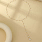 Flatlay of gold tone faux pearl backdrop lariat necklace with round pearls and a teardrop drop on cream