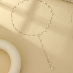 Flatlay of gold tone faux pearl backdrop lariat necklace with round pearls and a teardrop drop on cream