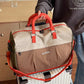 Beige and orange colorblock travel duffel with padded handles held over a white suitcase