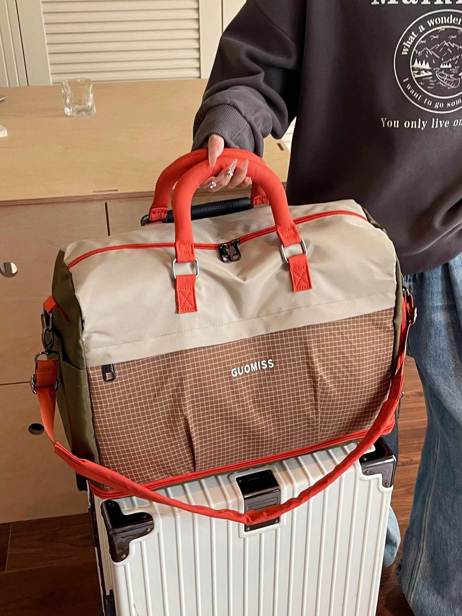 Beige and orange colorblock travel duffel with padded handles held over a white suitcase