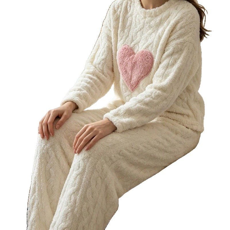 Woman seated in a cream plush fleece pajama set with a pink heart patch on a white background