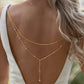 Gold tone layered back drop necklace falling down the open back of a model in white