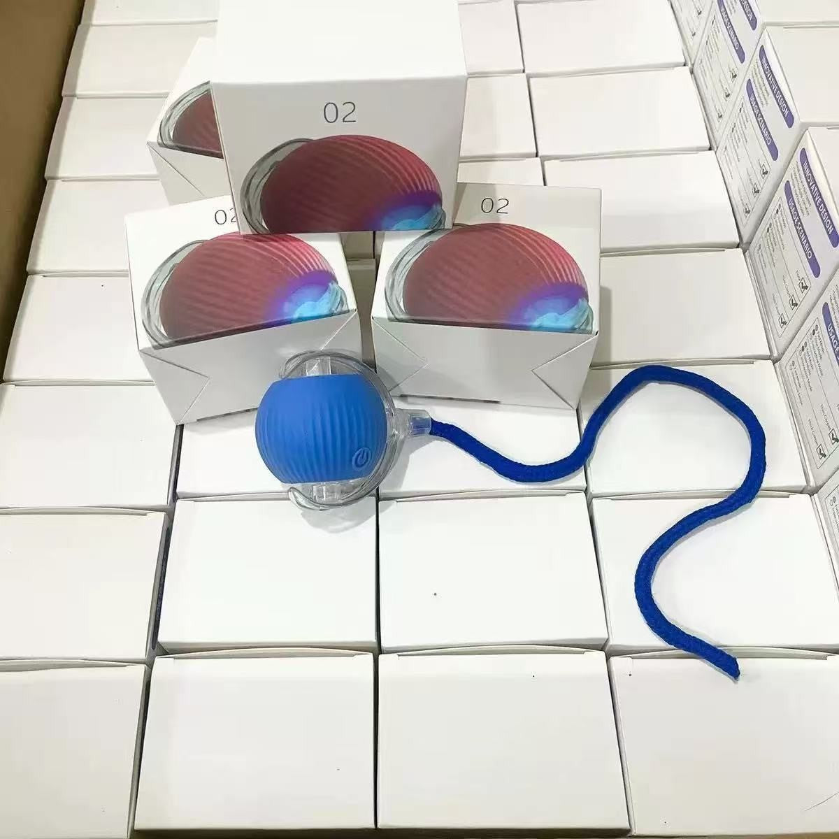 Blue silicone rolling cat ball with a blue rope tail resting on rows of white retail boxes