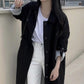 Black single breasted long trench coat worn open outdoors over white jeans