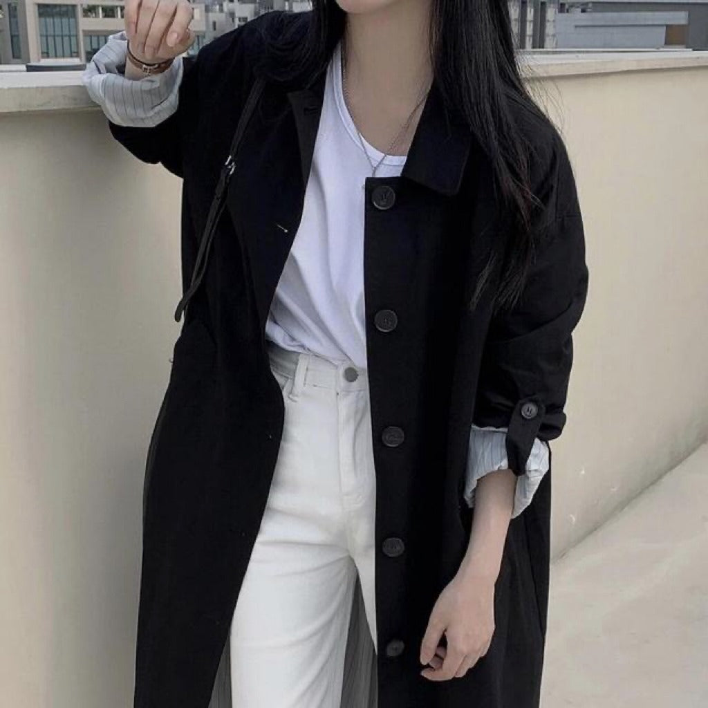 Black single breasted long trench coat worn open outdoors over white jeans