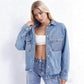 Woman holding the collar of an open light blue washed denim shirt with chest pockets over a white top