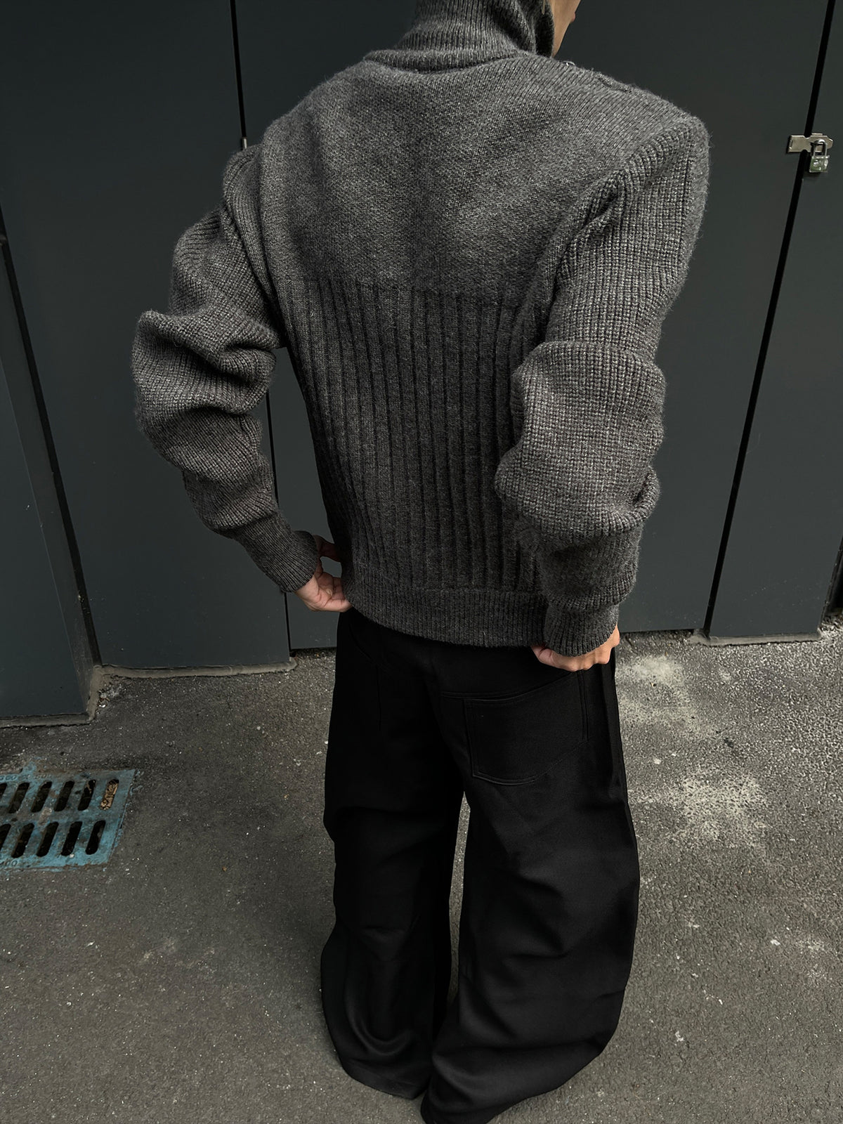 Back view of the gray ribbed knit cardigan on a man with hands in the trouser pockets, squared shoulders