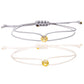 Gray and cream cord bracelets with gold tone charms laid flat as a matching pair