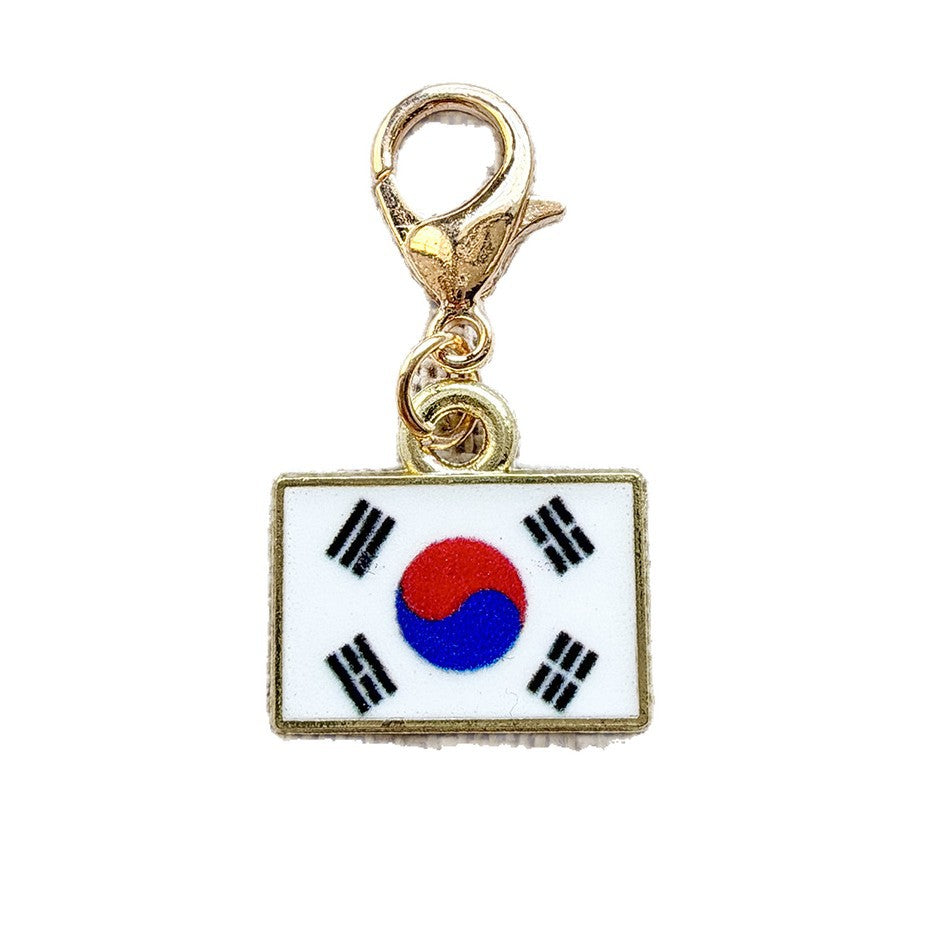 Enamel country flag keychain charms laid out, each a plate on a gold tone lobster clasp