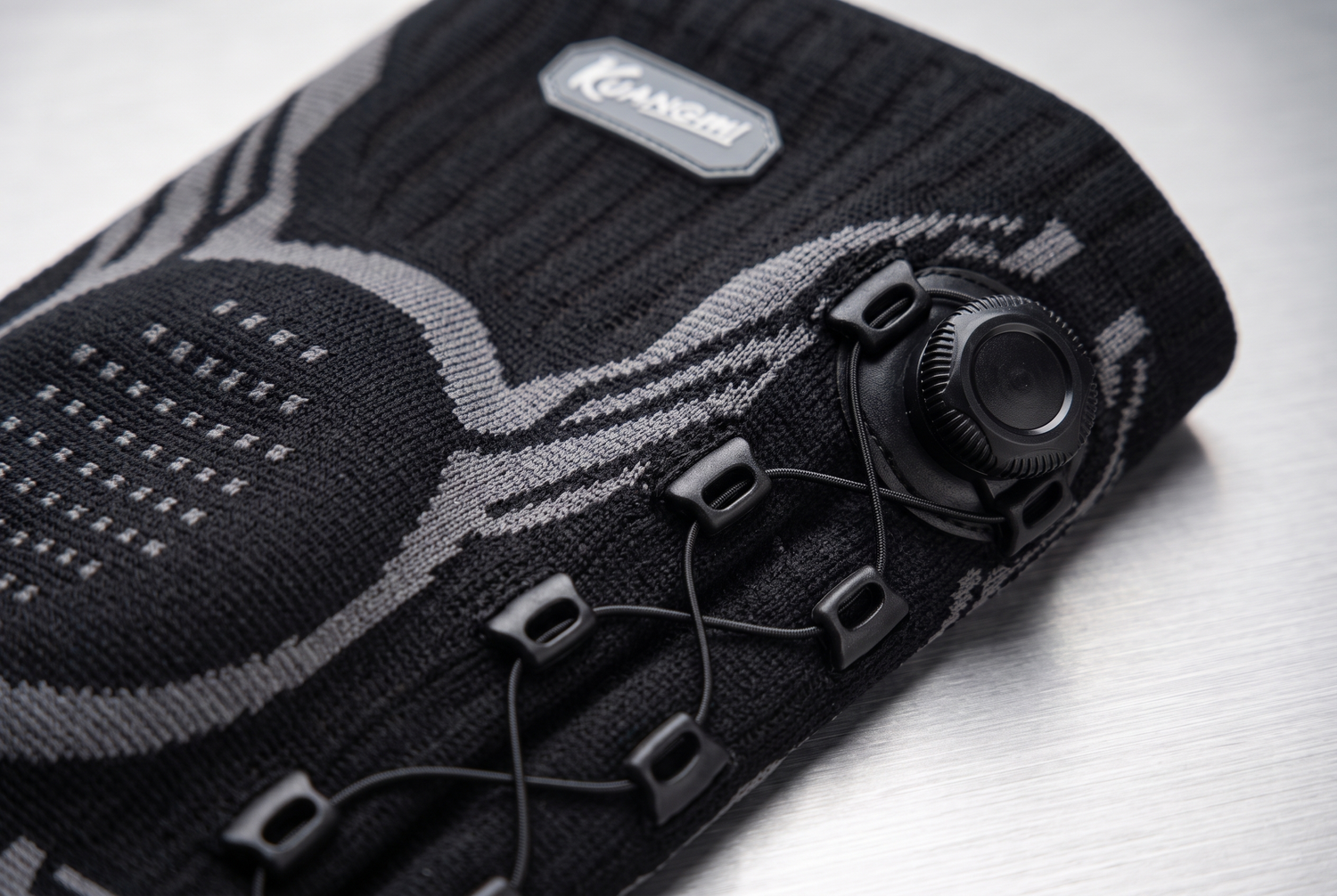 Macro close up of the KUANGMI knee sleeve rotary adjustment knob and crossed lacing