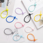 Group of tadpole shaped silicone cable ties in several solid colors laid flat on a light surface