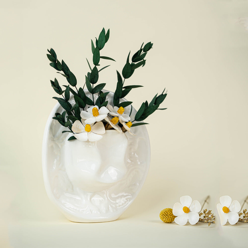 White ceramic cowboy hat vase with white blooms and greenery on a beige background