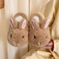 Pair of brown bunny plush slippers with pink lined upright ears held in a hand against cream fabric, view 5 of 5
